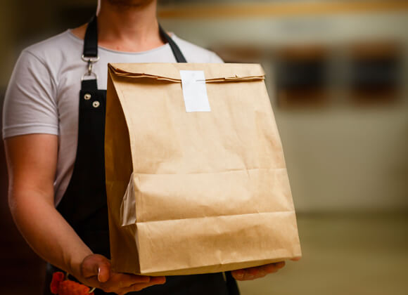 Man with apron is holding a paper bag