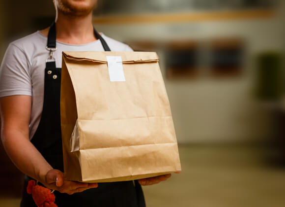 Human with apron is holding a paper bag